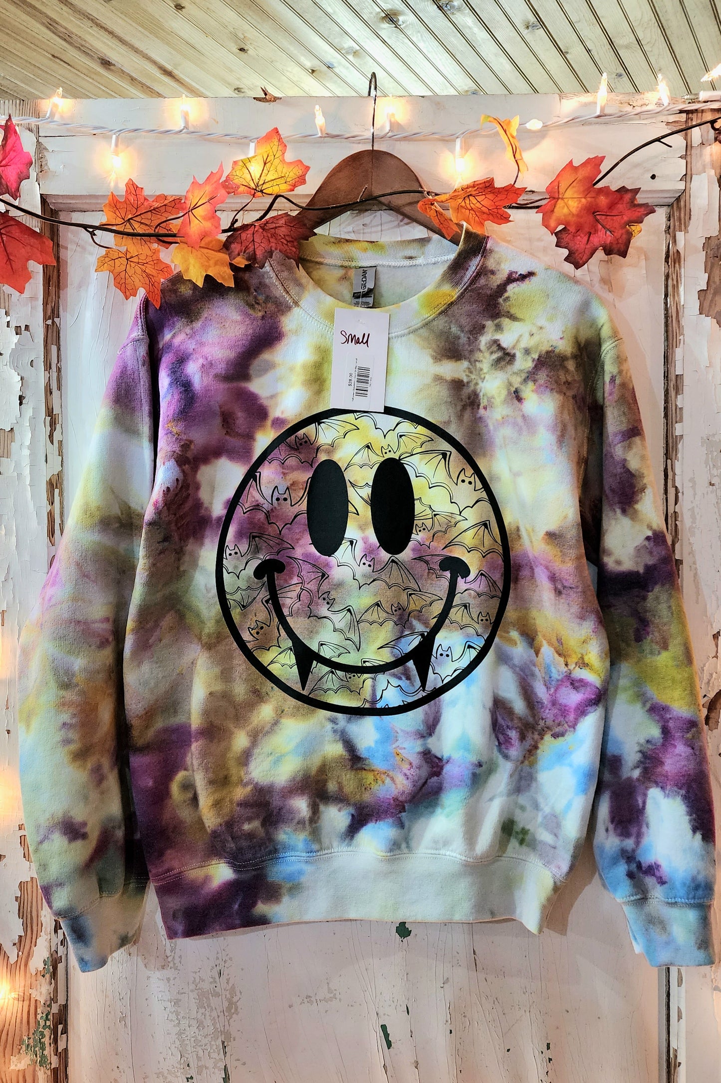 Tie dye sweat shirt in colors of brown, blue, purple, and hints of green. Large smiley face is pressed to the front with vampire teeth. Bat designs are contain in the smiley