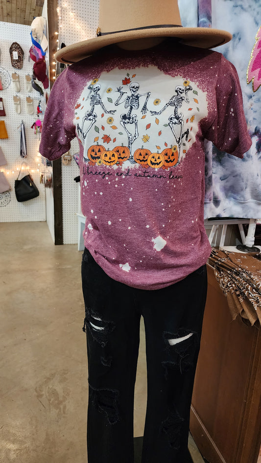 Shirt is burgundy with an image of three skeletons dancing in leaves. "Fall breeze leaves and autumn leaves" is written across thw bottom of image, right below jack o lanterns.